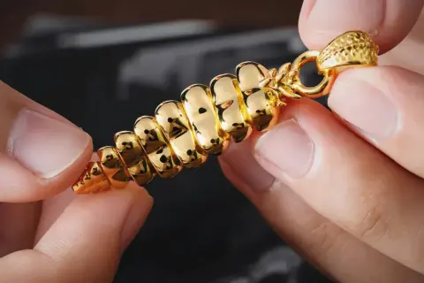Manos sostienen un colgante dorado brillante, con forma de espiga. ¿Cómo saber si es oro? Su brillo intenso y diseño detallado sugieren autenticidad.