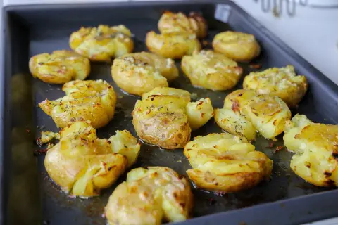Ugnsbakade smashed potatoes med ost och örter på en plåt. Krispiga och gyllene, redo att serveras.