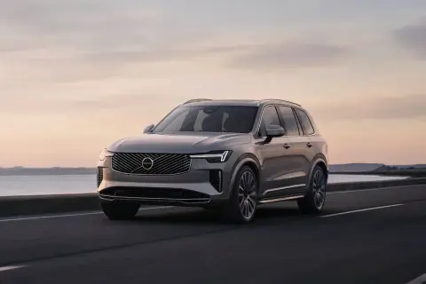 Elegancki Volvo XC90 T8 w kolorze szarym jedzie wzdłuż malowniczego wybrzeża o zachodzie słońca.