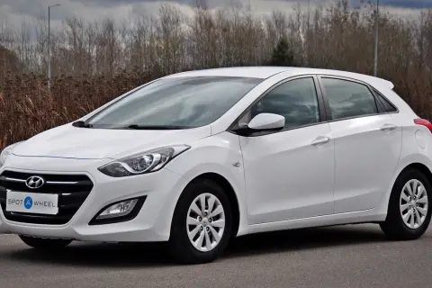 Biały Hyundai hatchback zaparkowany na drodze, z zaroślami w tle.