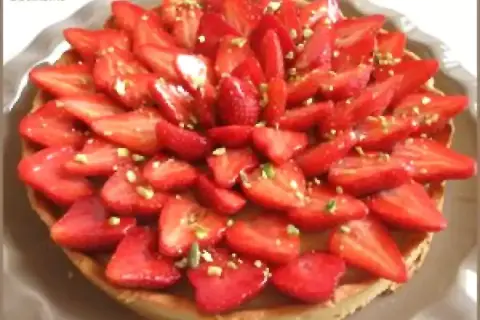 Tarte aux fraises fraîchement préparée, garnie de fraises coupées et de pistaches concassées. Un délice visuel et gustatif.