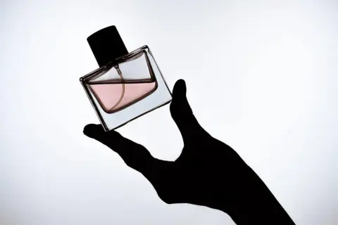 Czarna dłoń trzyma flakonik perfum z różowym płynem. To Twój **signature scent**, który podkreśla Twój styl.