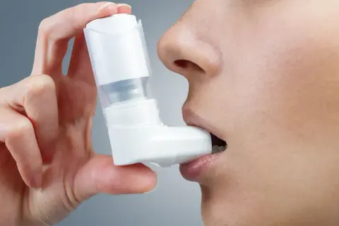 Kobieta używa inhalatora, który może zawierać najnowsze leki na astmę oskrzelową.