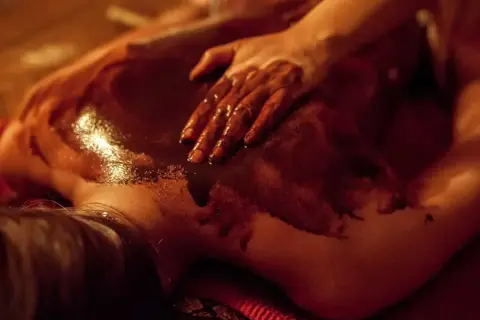 Dłoń masuje plecy pokryte czekoladą do masażu spa. Ciemna, błyszcząca masa rozpływa się na skórze, tworząc relaksującą atmosferę.