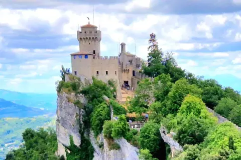 San Marino: en medeltida borg tronar på en klippavsats, omgiven av grönskande träd och med en vidsträckt vy över kullar och berg.