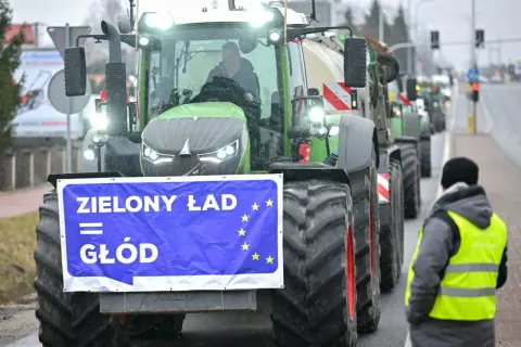 Traktor z banerem "Zielony Ład = Głód" i flagą UE, w tle protestujący rolnicy.