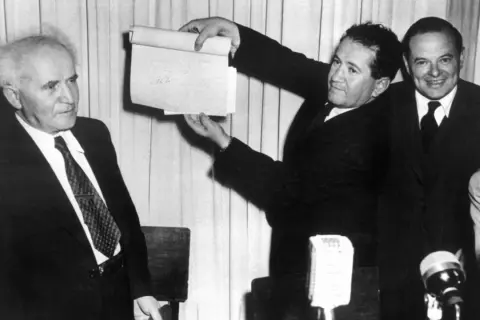 David Ben-Gurion hält ein Dokument hoch, das die Gründung Israels 1948 markiert.