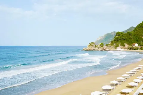 Piękna, piaszczysta plaża na Korfu z rzędami białych parasoli i turkusowym morzem.