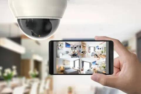Caméra de surveillance au plafond et smartphone affichant plusieurs flux vidéo, un type d'alarme moderne pour la sécurité domestique.