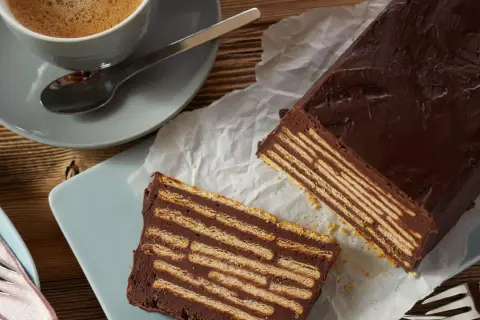 Schokoladiger kalter Hund, geschichtet mit Keksen, neben einer Tasse Kaffee.