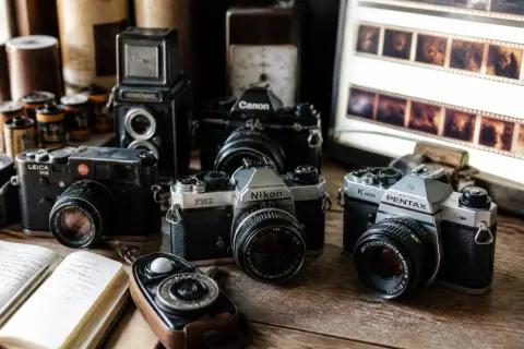Collection de vieux appareils photo argentiques, films et un livre ouvert, évoquant l'art de la photographie argentique.