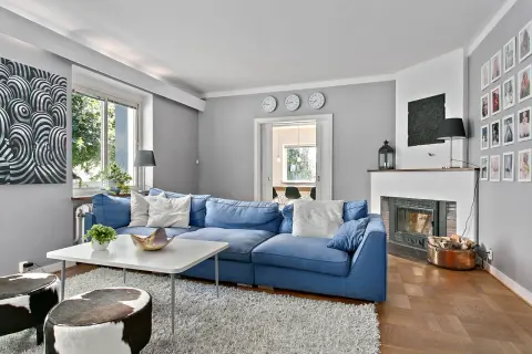 Blau passt toll zu seidengrau, wie dieses Wohnzimmer mit blauem Sofa, Kamin und Kuhfellhockern zeigt.