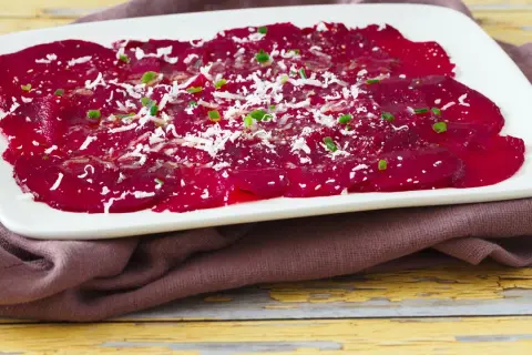 Rote Bete Carpaccio, hauchdünn geschnitten und mit Parmesan und Schnittlauch bestreut, auf einem weißen Teller.