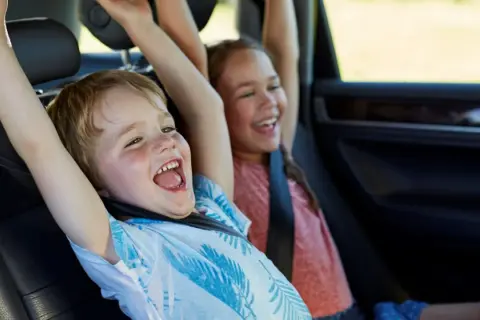 Niños emocionados en el coche, con los brazos en alto. Parecen haber alcanzado la altura mínima para no usar silla en el coche.