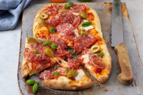 En härlig zeta pinsa med salami, oliver och färsk basilika, redo att avnjutas.