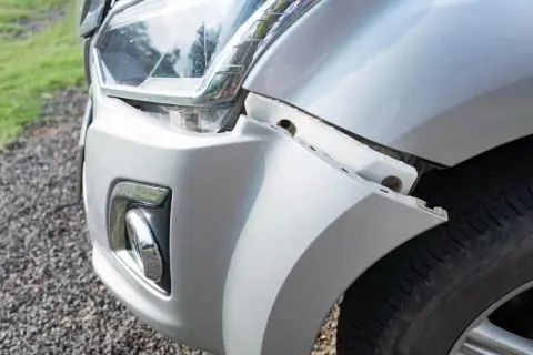 Le bouclier avant de la voiture est détaché, révélant des fixations et le pneu.