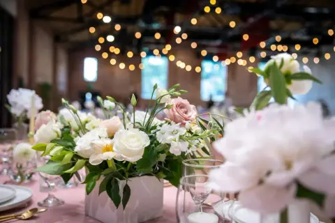 Un arrangement floral délicat, thème fleur, orne une table de réception rose. Des roses blanches et roses se mêlent à des fleurs plus petites et du feuillage vert.