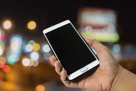 Dłoń trzyma smartfon Samsung. Dowiedz się, jak włączyć telefon Samsung, naciskając przycisk zasilania.