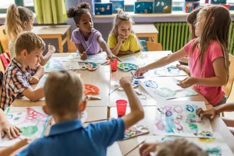 Niños y niñas disfrutan del arte en infantil, pintando con acuarelas y pinceles en una clase creativa.