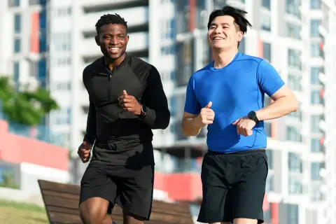 Deux hommes souriants courent ensemble dans un parc urbain. Ils semblent apprécier leur routine de courir tous les jours.