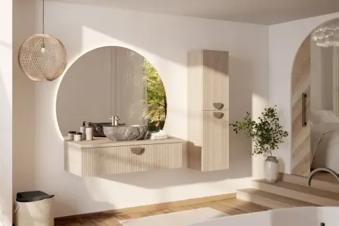 Une salle de bain moderne et chic avec un lavabo en pierre, un miroir rond lumineux et une armoire en bois clair. La lumière naturelle filtre à travers une fenêtre circulaire.
