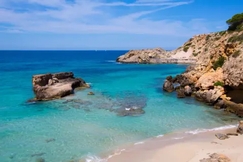 Aguas cristalinas y rocas escarpadas en una cala idílica. Unos pequeños **planes** se ven en el horizonte, invitando a soñar con esta **playa** paradisíaca.