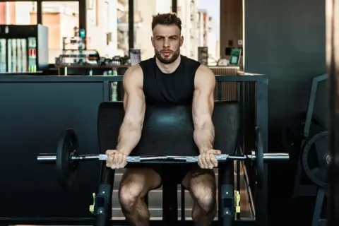 Mann trainiert Bizeps mit Langhantel im Fitnessstudio. Calisthenics-Liebhaber baut Muskeln auf.