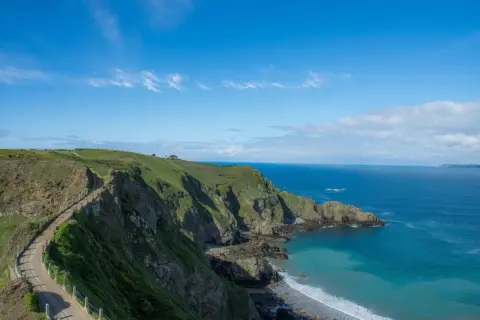 Chemin côtier verdoyant sur les falaises de Jersey, idéal pour visiter Jersey à pied. Mer bleue et ciel clair.