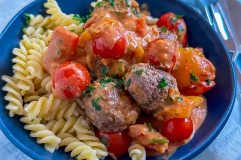 Herzhafte Hackfleisch Gerichte: saftige Hackbällchen in cremiger Tomatensoße mit Kirschtomaten und Fusilli-Nudeln, garniert mit frischer Petersilie.