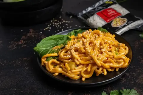 Pyszne tantanmen z grubym makaronem, polane kremowym sosem, posypane sezamem i podane z zielonymi liśćmi.