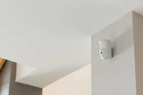 Détecteur de mouvement blanc fixé dans un coin, prêt à fabriquer une alarme.