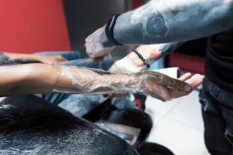 Tätowierer wickelt Arm in Folie, um das frische Tattoo zu schützen. Die Haut brennt leicht, aber das Kunstwerk wird bald sichtbar sein.