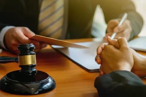 Sędzia z młotkiem i dokumentami, prawnik pisze, klient z modlącymi się dłońmi. Rozważana sankcja kredytu darmowego.