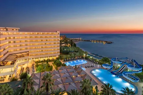 Oświetlony hotel Ozkaymak Select Resort Hotel z basenami i zjeżdżalniami wodnymi nad morzem o zachodzie słońca.