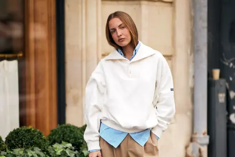 Frau kombiniert lässig ein gestreiftes Hemd mit einem weißen Pullover, der wie ein Hoodie wirkt.