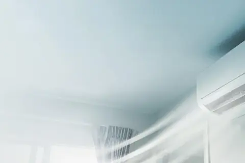 En vit luftkonditioneringsenhet på en vägg blåser ut sval luft. Snabb installation av AC för ett behagligt inomhusklimat.