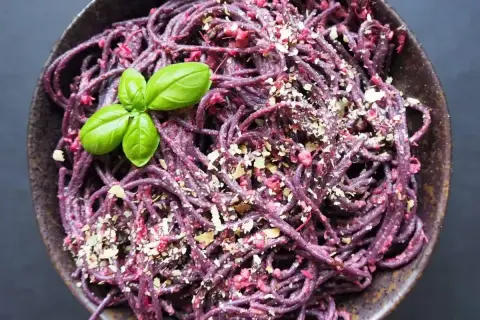 Fioletowy makaron z pesto z buraków, posypany orzechami i udekorowany listkami bazylii.