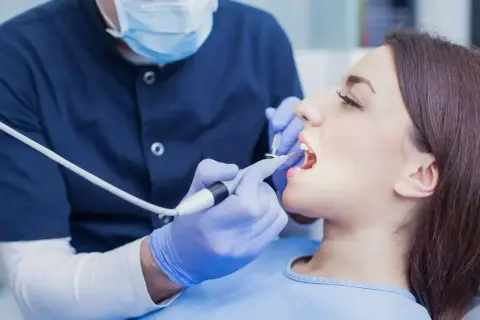 Dentysta bada zęby pacjentki. Zastanawiasz się, ile kosztuje wizyta u dentysty?