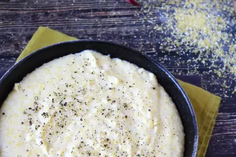 Kremowa polenta w czarnej patelni, posypana świeżo mielonym pieprzem, na drewnianym tle.