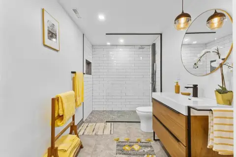 Salle de bain en longueur moderne avec douche carrelée, vasque en bois et serviettes jaunes vives.
