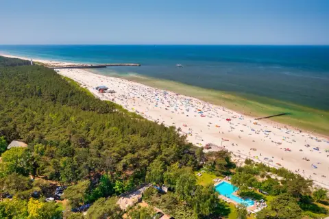 Słoneczne plaże w Polsce tętnią życiem. Tłumy plażowiczów, zielony las i błękitne morze tworzą wakacyjny krajobraz.