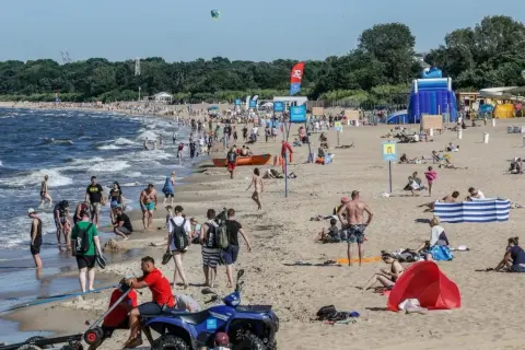 Tłum ludzi na piaszczystej plaży nad Bałtykiem w słoneczny dzień.