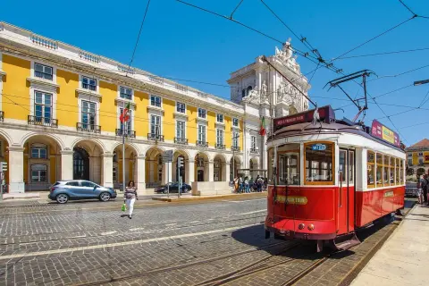 Czerwony tramwaj w Lizbonie, obok żółtego budynku z arkadami. Czy do Portugalii potrzebny jest paszport? Warto sprawdzić przed podróżą!