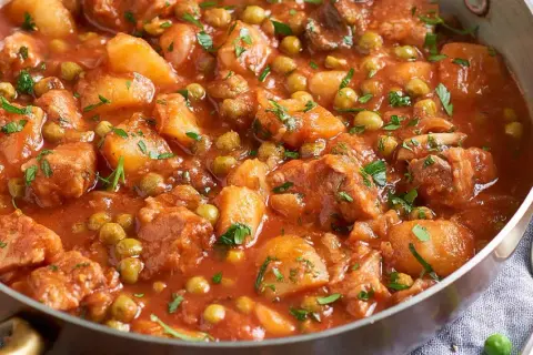 Un saporito spezzatino di vitello con piselli e patate, cotto in un sugo rosso e guarnito con prezzemolo fresco.