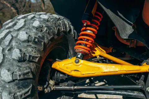 Gros plan sur la jambe de force voiture, avec son amortisseur orange vif et son pneu tout-terrain. Le bras de suspension jaune vif est prêt pour l'aventure.