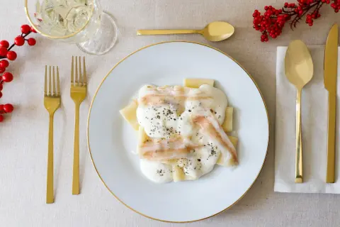 Piatto di paccheri conditi con una cremosa spuma di pecorino e guarniti con pepe nero. Accanto, posate dorate e un rametto di bacche rosse.