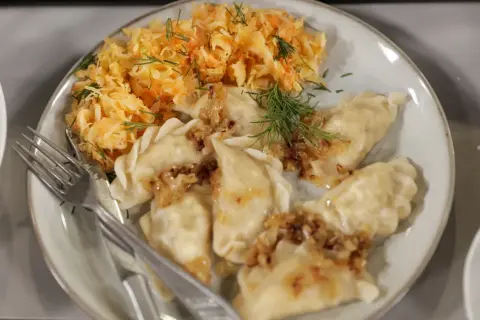 Pyszne pierogi z cebulką i koperkiem, podane z surówką z kiszonej kapusty. Idealne na mandu menu.