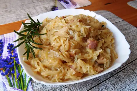 Pyszna kapusta zasmażana z boczkiem, podana na białym talerzu, ozdobiona gałązką rozmarynu.