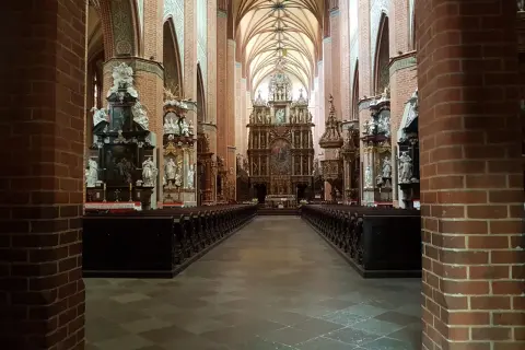 Wnętrze katedry w Pelplinie z rzędami ławek i bogato zdobionym ołtarzem głównym.