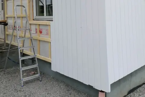 Byggarbetsplats där man valt att kombinera liggande och stående panel på husfasaden. En stege står redo.